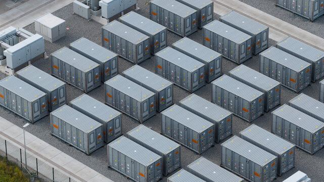 Aerial view of a battery energy storage system with rows of grey shipping-container-style battery units arranged on a gravel surface in Espel, Flevoland, Netherlands.