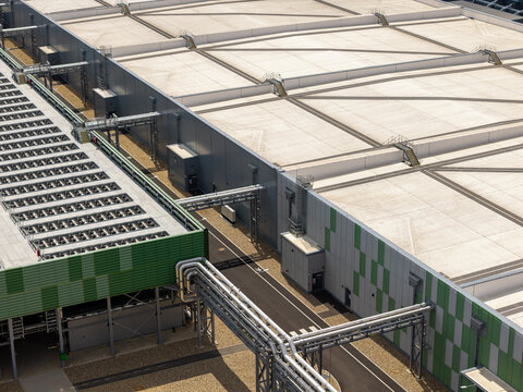 Aerial view of a modern data center facility featuring extensive cooling infrastructure, complex piping systems, and large flat rooftops in the United Kingdom.