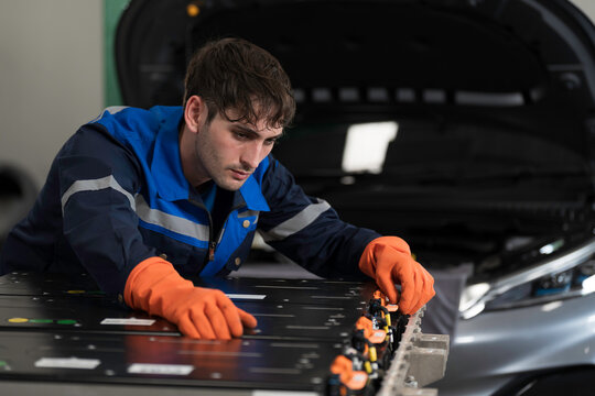 EV car maintenance garages. Technician diagnosing electric car vehicles battery, high-voltage battery service and general electric vehicle care at auto workshop