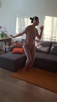 Woman dances in living room while wearing headphones during afternoon