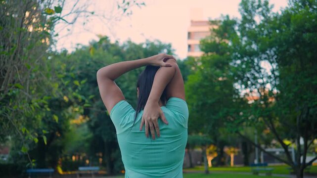 Woman, stretching and triceps warm up in park with fitness, morning routine or wellness outdoor. Back view, person or athlete with arms overhead for flexibility, exercise prep and workout in city.