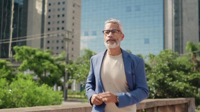 Mature Brazilian businessman with gray beard and glasses running late checking wristwatch in modern urban city park