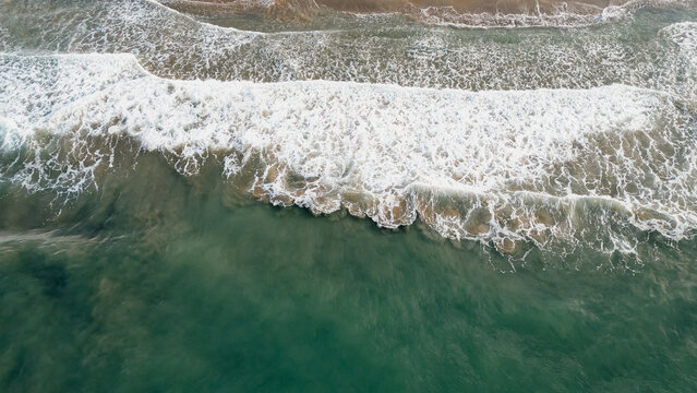 Top down aerial view of emerald sea waves washing ashore with white foam on sandy beach in Greece for ocean nature travel stock photo background concept texture