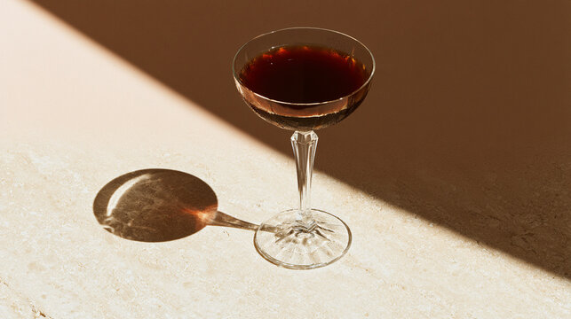 Dark cocktail in coupe glass casting shadow in sunlight