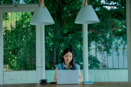 Young Asian woman talking on smartphone while working on laptop in modern workspace