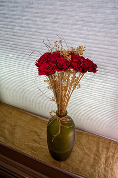 A vase of artificial red roses backlit on a windowsill