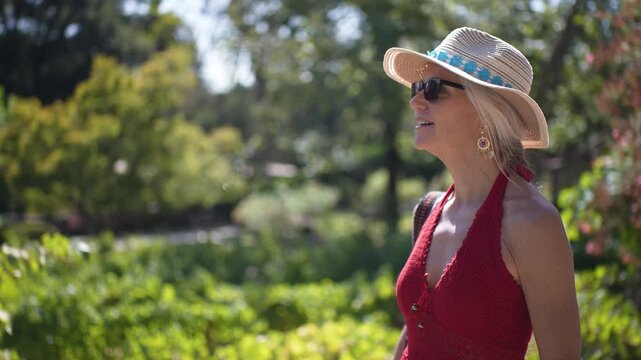 A senior woman walks through a vineyard in Napa, smiles, and enjoys the sunny weather during a wine tour in California.