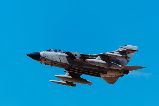 Albacete, Spain - June 12, 2026: A military fighter jet aircraft flying against a bright blue sky, showcasing its combat design and underwing fuel tanks over Los Llanos Air Base