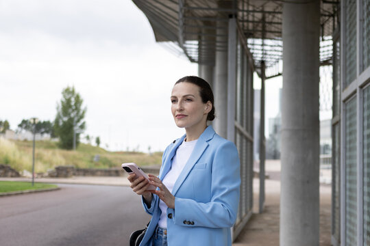Businesswoman holding a smartphone waiting for public transport at a bus stop
