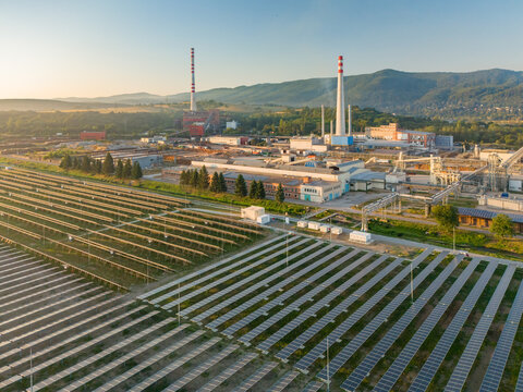 Aerial view of a solar farm installed at the Kronospan industrial facility with factory buildings, tall chimneys, and green hills in Zvolen, Banska Bystrica Regio, Slovakia.