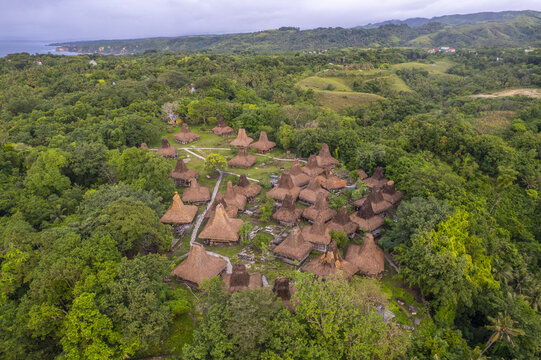 Aerial view of Yaro Wora traditional village with distinctive thatched-roof houses nestled in lush tropical forest and rolling hills in Lamboya, Sumba, Indonesia.