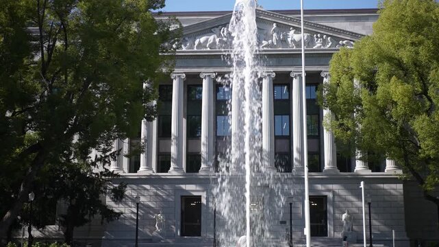 View of California State Office Building with a fountain and green trees. Bright sunlight illuminates the facade of the building.