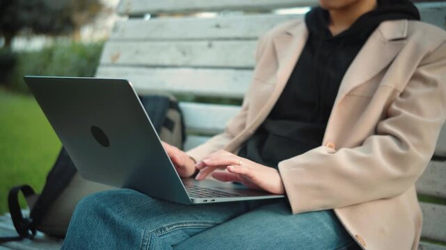Close-up of a young woman's hands using a laptop in an urban setting, showing remote work, technology, and modern digital lifestyle.
