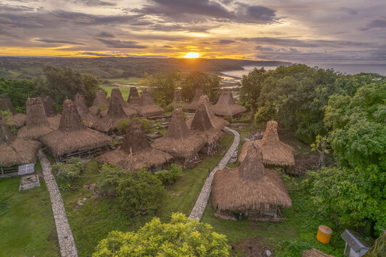 Aerial view of Yaro Wora traditional village with tall thatched-roof houses and stone paths surrounded by lush greenery at sunset in Lamboya, Sumba, Indonesia.
