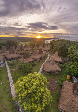 Aerial view of Yaro Wora traditional village with distinctive high-pitched thatched roofs, stone pathways, and lush greenery at sunset in Lamboya, Sumba, Indonesia.