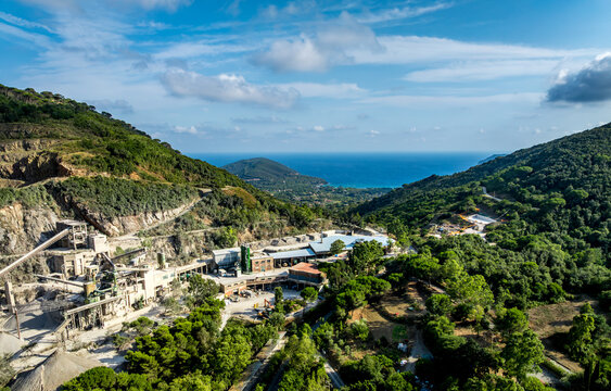 Aerial view of Cava di Colle Reciso quarry in the green hills of Elba island with industrial machinery and stone processing facilities, Portoferraio, Toscana, Italy.