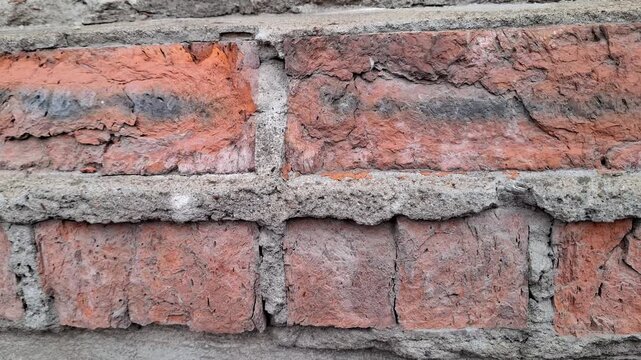 Weathered red brick wall with aged mortar and rough texture, rustic architecture, historic construction, urban background, durable building material.