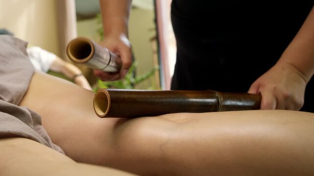 creole bamboo massage. Professional spa therapist uses bamboo sticks for relaxing leg massage treatment. Traditional percussion method supports recovery and body wellness.