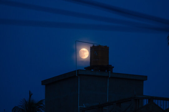 The July Full Moon is known as the ''Buck Moon'' in Native American tradition, coinciding with Guru Purnima. See black storm clouds, tree branches, electric wire, and construction,  lunar corona  