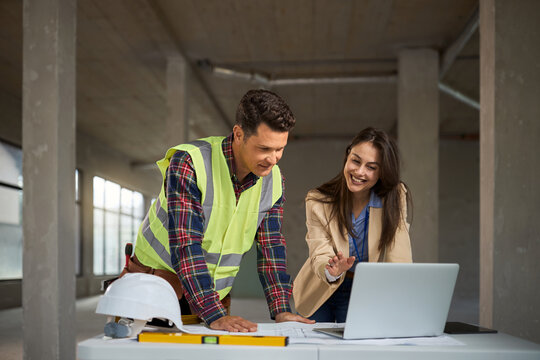 Female real estate developer and her worker using laptop at construction site