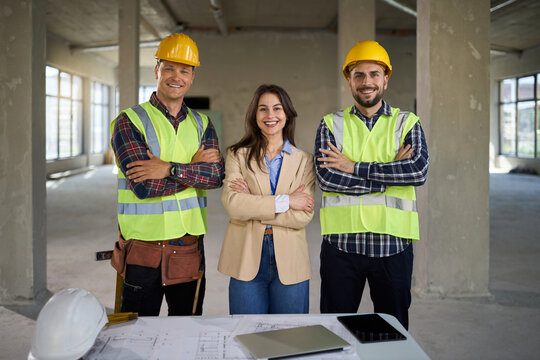 Happy female architect standing with crossed arms alongside her workers at a construction site and looking at the camera.