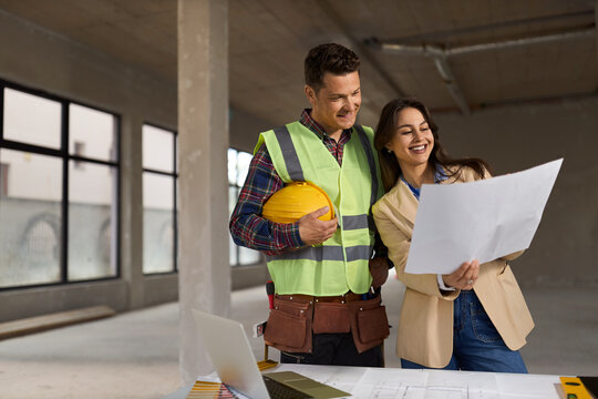 Female building contractor  and manual worker cooperating while working on blueprints at construction site