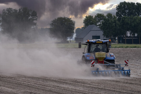Rear view of  Blue Tractor Working on Dry Dusty Farmland