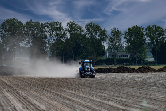 Blue tractor working on dry dusty farmland, raising dust while cultivating a field in rural agricultural landscape