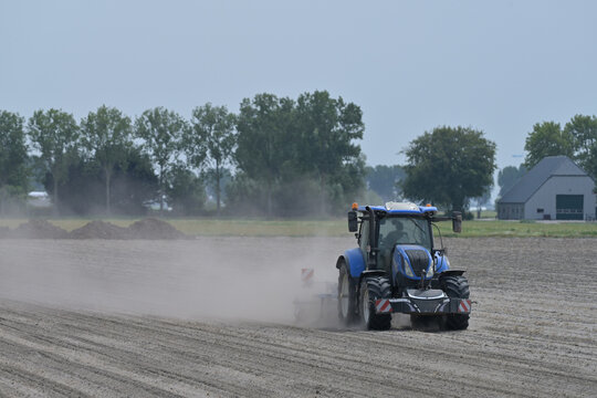 Blue tractor working on dry dusty farmland, raising dust while cultivating a field in rural agricultural landscape