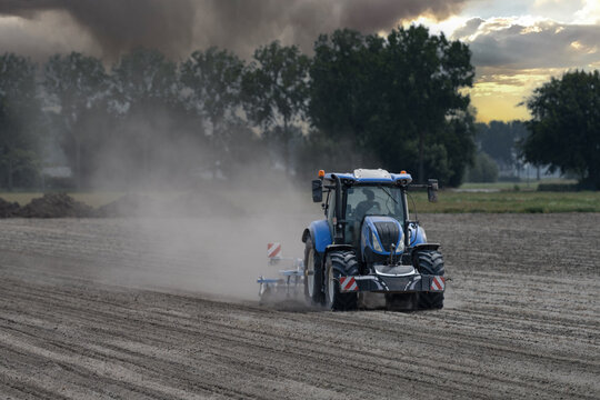 Blue tractor working on dry dusty farmland, raising dust while cultivating a field in rural agricultural landscape