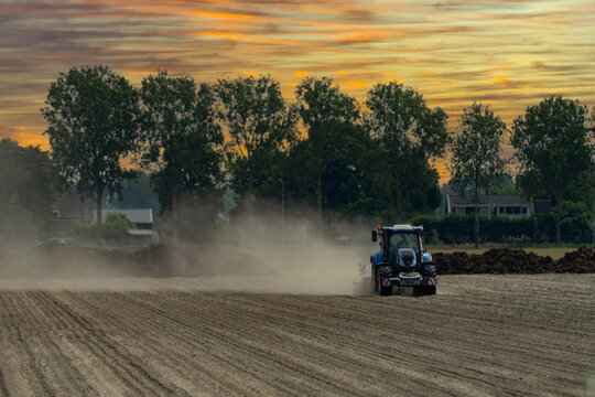 Blue tractor working on dry dusty farmland, raising dust while cultivating a field in rural agricultural landscape