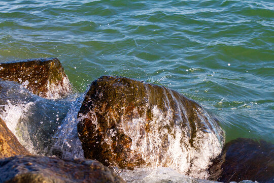 Horizontal eye level close up shot of sea waves splashing against large coastal rocks