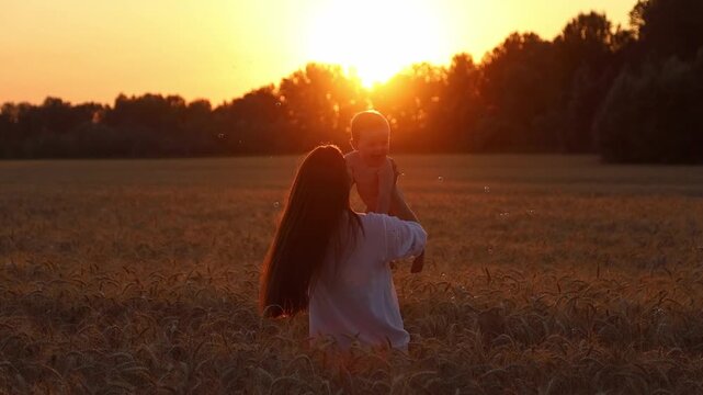 A happy mother and her seven-month-old son spin in a wheat field in the rays of the setting sun against a backdrop of soap bubbles