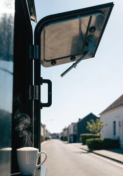 Coffee truck on street concept. A steaming cup of coffee sits on a windowsill of a vehicle with the window open, overlooking a quiet residential street.