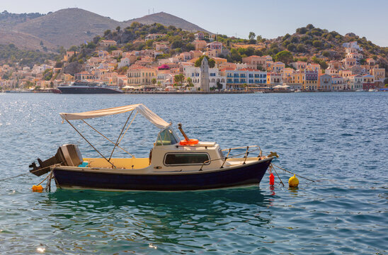 Small motor boat anchored in the bay with the colorful waterfront of Symi Island, Dodecanese, Greece, in the background.