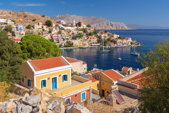 View of the waterfront with the historic clock tower and colorful hillside houses in Symi Harbor, Dodecanese, Greece.
