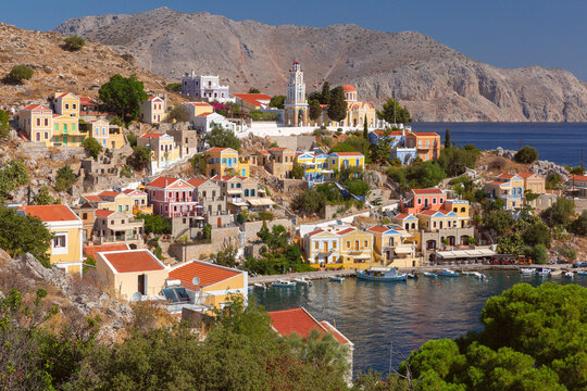 View of the waterfront with the historic clock tower and colorful hillside houses in Symi Harbor, Dodecanese, Greece.