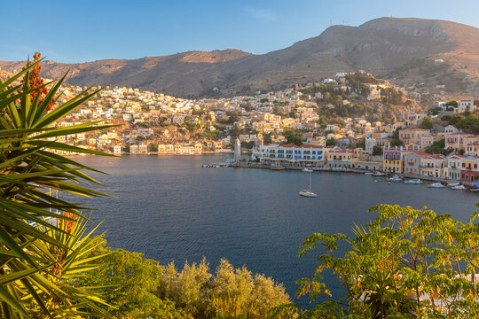 Elevated view of Symi Harbor with colorful waterfront buildings, hillside houses, and surrounding mountains on Symi Island, Dodecanese, Greece.