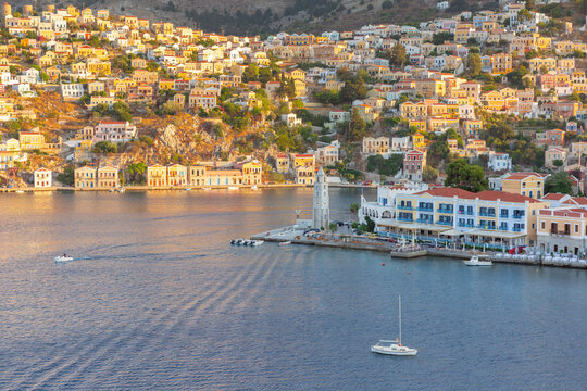 Elevated view of Symi Harbor with colorful waterfront buildings, hillside houses, and surrounding mountains on Symi Island, Dodecanese, Greece.