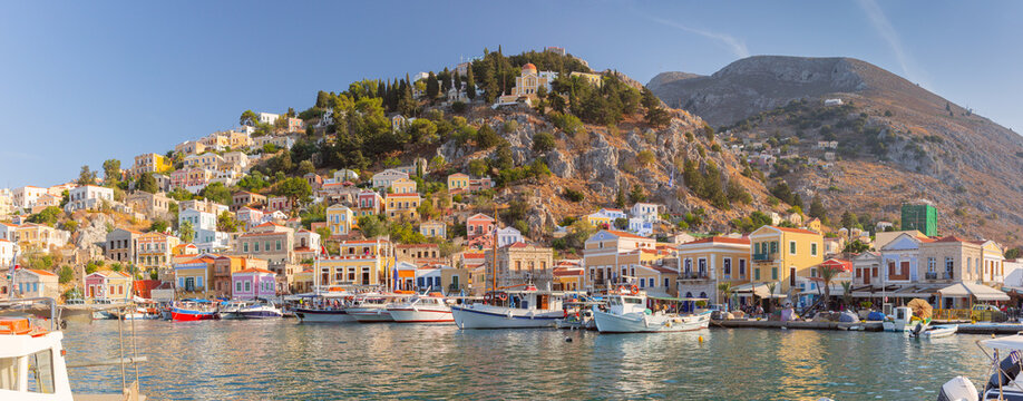 Panoramic view of Symi Harbor with colorful neoclassical houses, yachts, and rocky hills on Symi Island, Dodecanese, Greece.