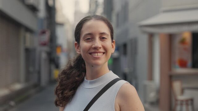 Portrait of a happy young caucasian woman with curly hair smiling and looking at the camera, standing in a traditional narrow alley during her vacation trip to Tokyo, Japan