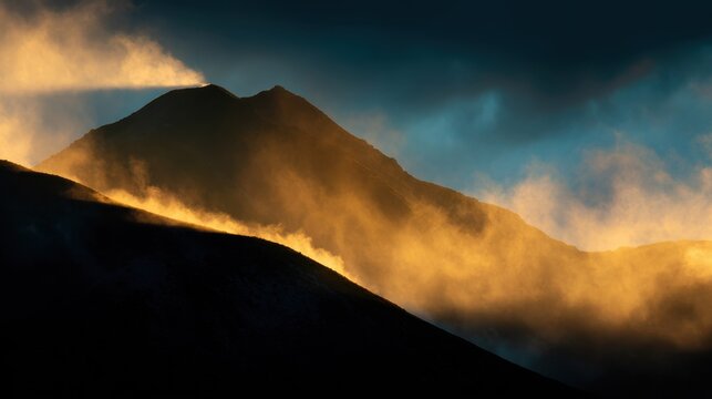 Dramatic mountain silhouette surrounded by glowing mist during sunrise with golden atmospheric light