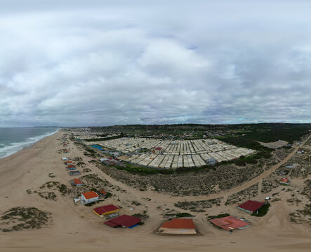 Aerial view of Praia da Mata beach featuring a large camping site with rows of structures nestled among coastal dunes along the Atlantic coastline in Costa de Caparica, Setubal, Portugal.