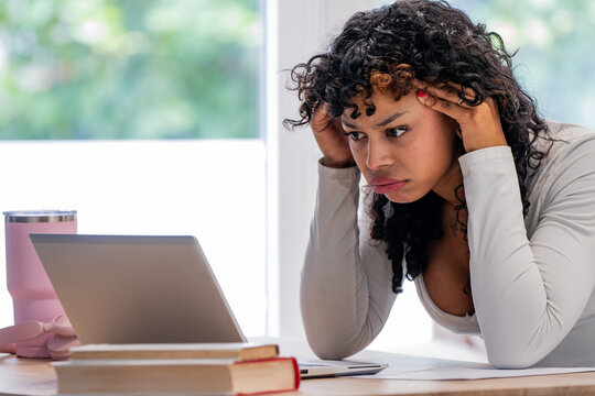 Young woman at a desk with a laptop, looking stressed and focused while studying or working
