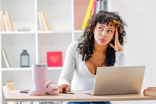 Young woman at a desk with a laptop, looking stressed and focused while studying or working