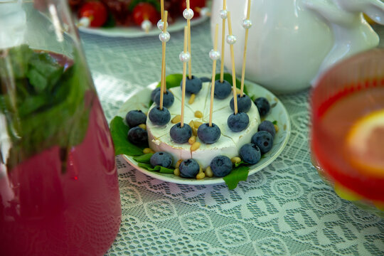 Elegant gourmet cheese plate garnished with fresh blueberries and decorative skewers. A refreshing pink drink and appetizers complete the stylish table setting