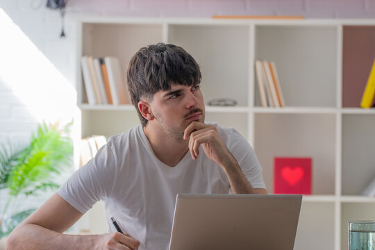 Young student at their home desk with a laptop and a thoughtful expression, working remotely or studying online