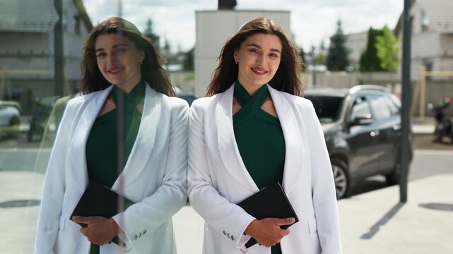Beautiful young business woman standing outdoors with her reflection in glass window