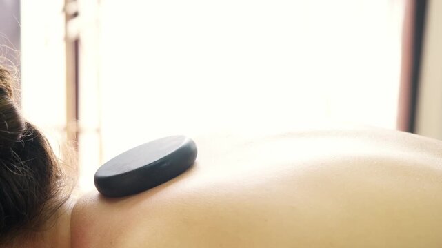 Close up shows therapist arranging smooth basalt stones on back for hot stone therapy. Natural heat supports muscle recovery and wellness care.