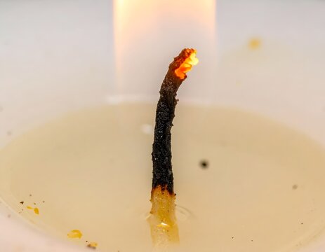 Macro close-up of a glowing lit candle wick burning in melted wax